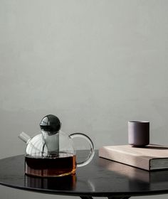 a glass tea pot sitting on top of a table next to a book and cup