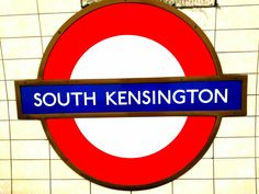 a blue and red sign that reads south kensington station on it's side in front of a tiled wall