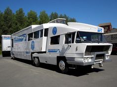 a large white bus parked in a parking lot next to some trees and other vehicles