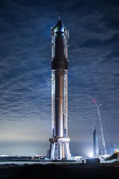 a very tall tower sitting in the middle of a field at night with lights on it