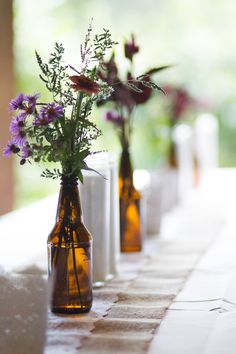 three vases with flowers are lined up on a long tableclothed table cloth