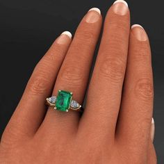 a woman's hand holding an emerald and diamond ring