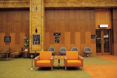 an orange couch and two chairs in front of a wooden paneled wall with signs on it