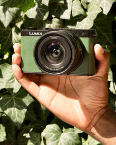 a person holding up a camera in front of some leaves