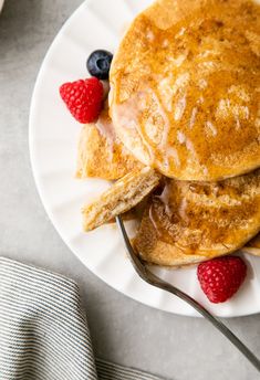 pancakes with syrup and raspberries on a white plate