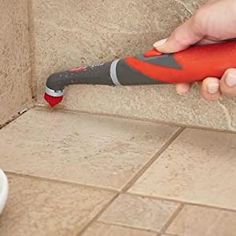 a person using a tile grouter to clean a bathroom floor with a red and gray tool