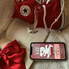 a pair of red converse shoes sitting next to an open book with a bow on it