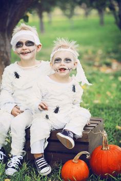 two young children dressed up in halloween costumes sitting on a crate with their faces painted white