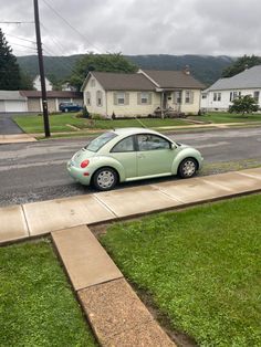 a small green car is parked on the side of the road in front of some houses