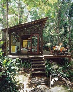 a small cabin in the woods with stairs leading up to it's deck area