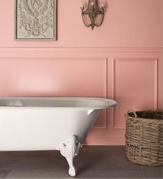 a white bath tub sitting next to a wall with pink walls and a basket on the floor