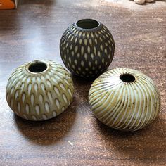 three vases sitting on top of a wooden table next to each other and one has a hole in the middle