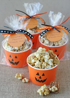 three orange buckets filled with popcorn and decorated with pumpkin faces for halloween party favors