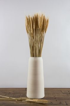 a white vase filled with dry grass sitting on top of a wooden table next to two golden straws