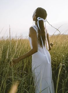 a woman in a white dress standing in tall grass with her hair blowing in the wind