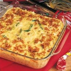 a casserole dish sitting on top of a red cloth covered table next to bread