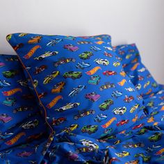 a blue bed topped with lots of pillows covered in cartoon cars on it's sides