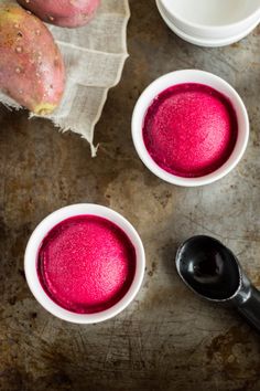 three white bowls filled with pink colored food next to two black spoons on a table