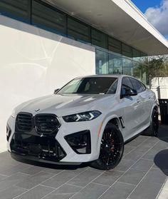 a white bmw suv is parked in front of a building with black wheels and rims