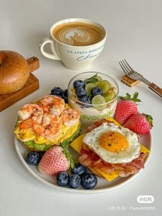 a white plate topped with breakfast foods next to a cup of coffee and bagel