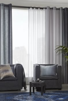 a living room with two gray chairs and a blue rug in front of the window