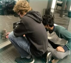 two men sitting on the ground looking at a cat's reflection in a mirror