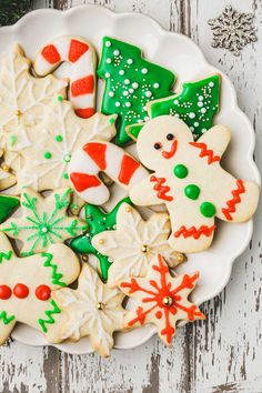 a plate full of decorated christmas cookies on top of a white wooden table with snowflakes