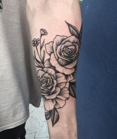 a woman's arm with roses on it and leaves in the middle, while she is wearing a white t - shirt