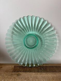 a green glass plate sitting on top of a wooden table next to a white wall