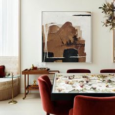 a dining room with red chairs and a painting hanging on the wall above it's table