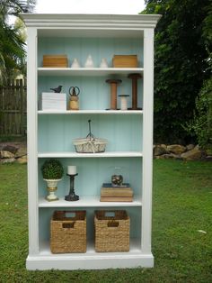 a white bookcase with baskets and books on it in the grass next to a fence