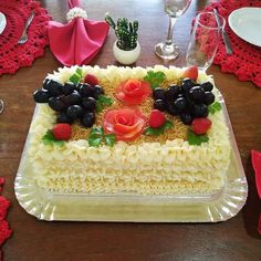 a cake with fruit and flowers on it sitting on a table next to wine glasses