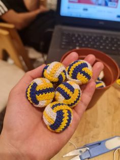 a person holding several small crocheted balls in front of a laptop computer on a table