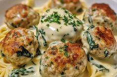 some meatballs and cheese are in a white sauce on top of pasta with spinach