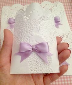 a hand holding a card with a purple bow on it and lace doily around the edges