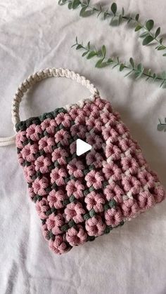 a crocheted purse sitting on top of a bed next to a green plant