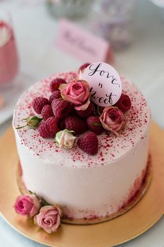 a white cake topped with raspberries and pink flowers on top of a gold plate