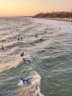 many people are swimming in the ocean at sunset or sunrise, with one person laying on his surfboard