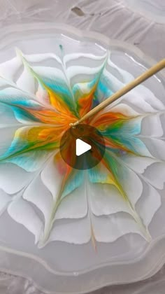 a colorful flower on a white plate with a wooden stick