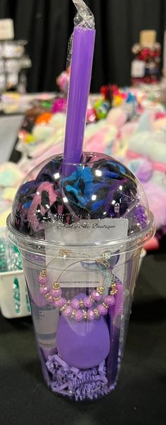 a purple candle in a plastic container with beads and other items around it on a table