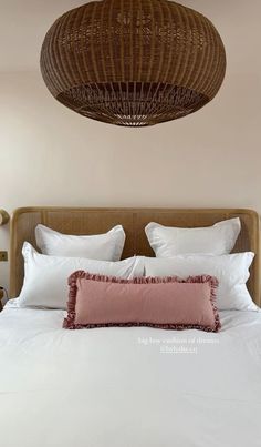 a bed with white sheets and pillows under a wicker light fixture over the headboard