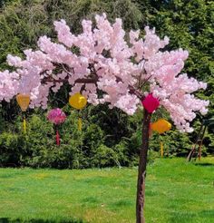 a pink tree with lots of colorful decorations on it's branches in the grass