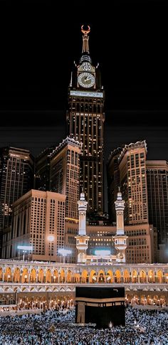 a large clock tower in the middle of a city with tall buildings behind it at night