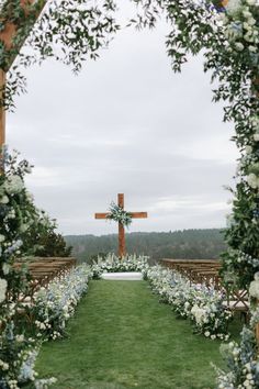 an outdoor ceremony with white flowers and greenery on the grass, in front of a wooden cross