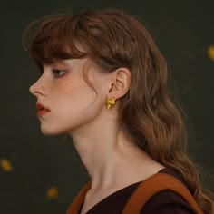 a woman with brown hair wearing gold earring on her left ear and looking off into the distance