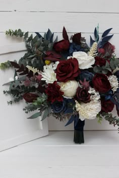 a bridal bouquet with red, white and blue flowers on a wooden bench in front of a door