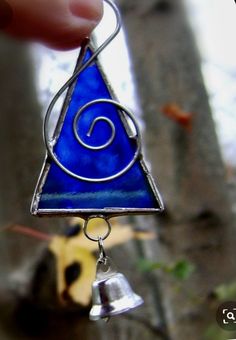 a hand holding a small blue triangle shaped glass piece with a bell hanging from it's side