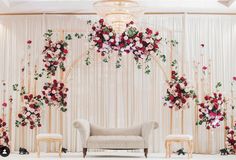 a couch sitting under a chandelier with flowers on the wall and chairs around it