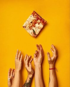 four hands reaching up towards a piece of pizza on a yellow background with one hand in the air