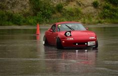 a red sports car driving down a wet road next to an orange cone on the ground